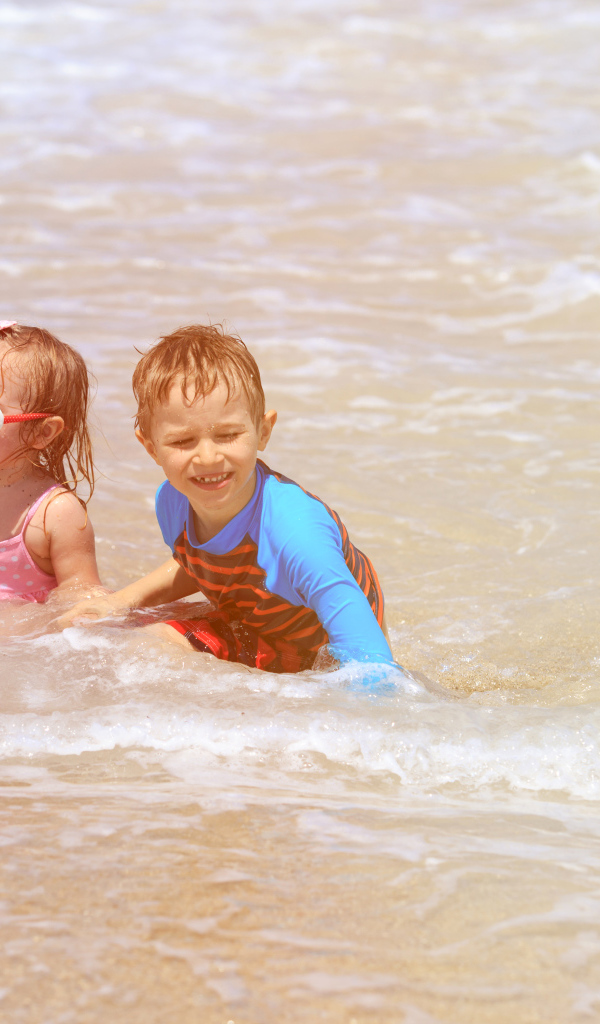 Маленькие мальчик и девочка купаются в море 