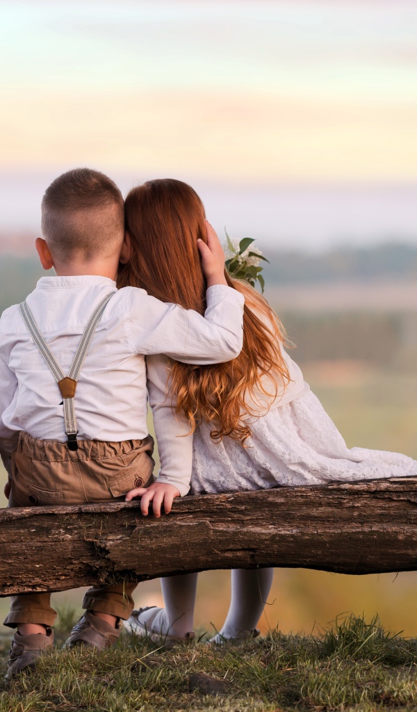 Маленькие мальчик и девочка обнимают друг друга на лавке