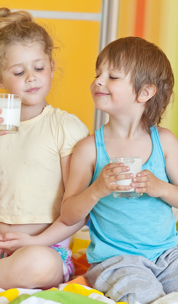 Маленькие мальчик и девочка со стаканами молока в руках 