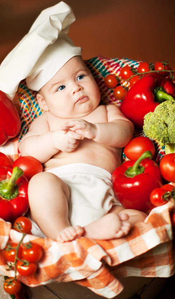 Маленький мальчик в костюме повара в корзине с перцем и помидорами