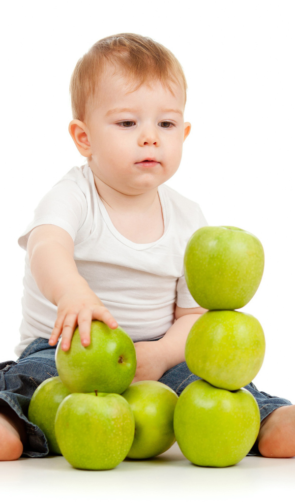Маленький мальчик играет с зелеными яблоками на белом фоне