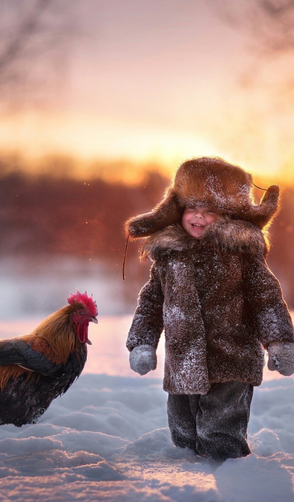 Маленький мальчик с петухом на снегу зимой