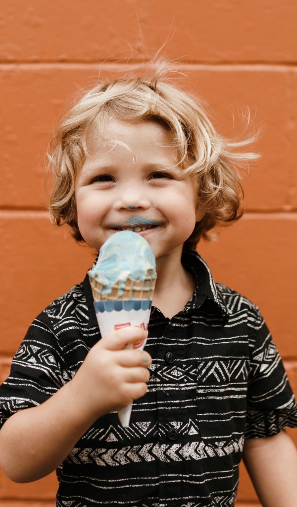 Маленький мальчик с мороженым в руках у стены