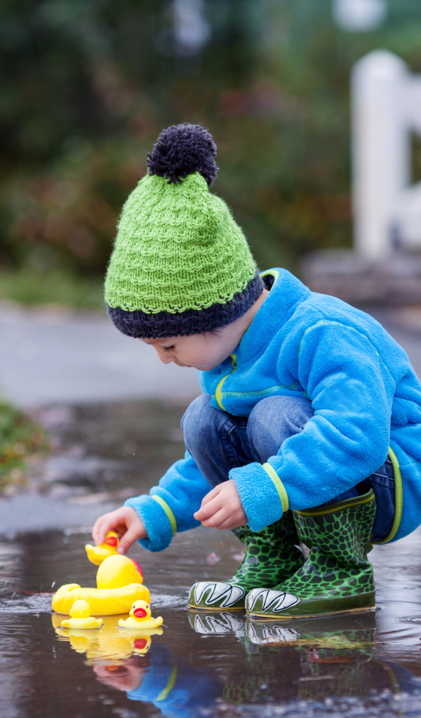 Маленький мальчик с резиновыми уточками в луже осенью