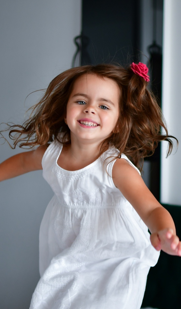 Маленькая веселая девочка в белом платье