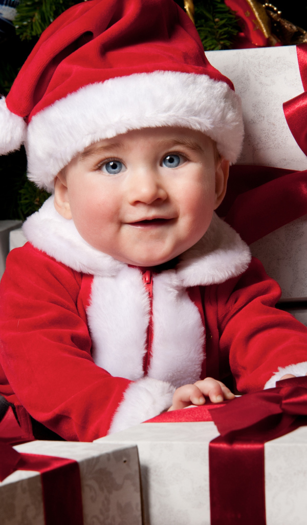 Маленький забавный голубоглазый ребенок в костюме Санты сидит на подарках