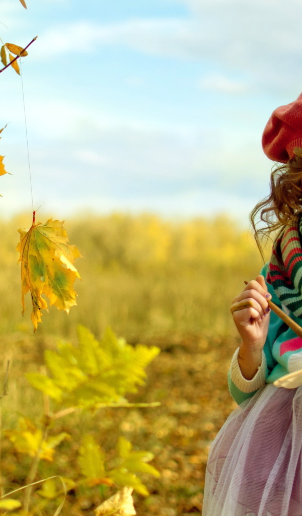 Маленькая девочка рисует красками на листьях осенью 