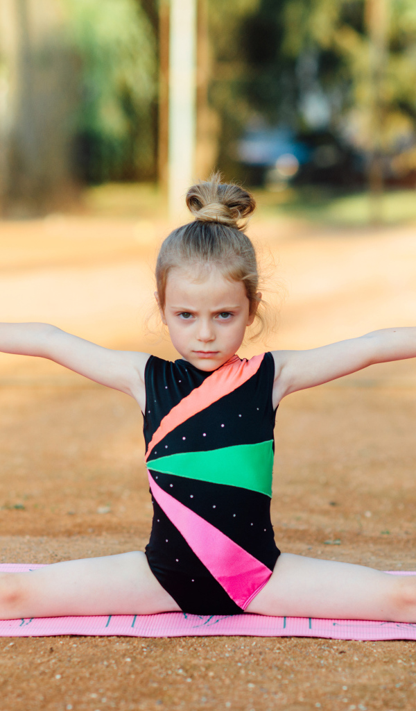Маленькая девочка гимнастка сидит на шпагате 