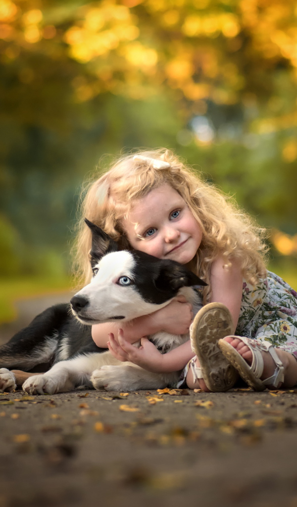 Маленькая девочка обнимает собаку на дороге осенью