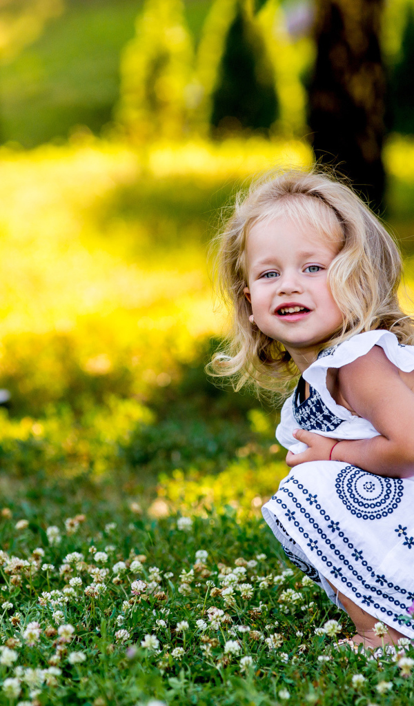 Маленькая девочка в красивом платье сидит на зеленой траве