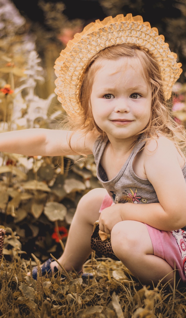 Маленькая девочка в шляпе сидит на траве с корзиной