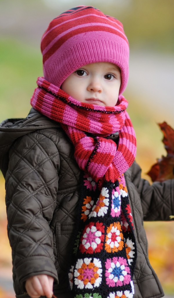 Маленькая девочка в розовой шапке с листьями в руке