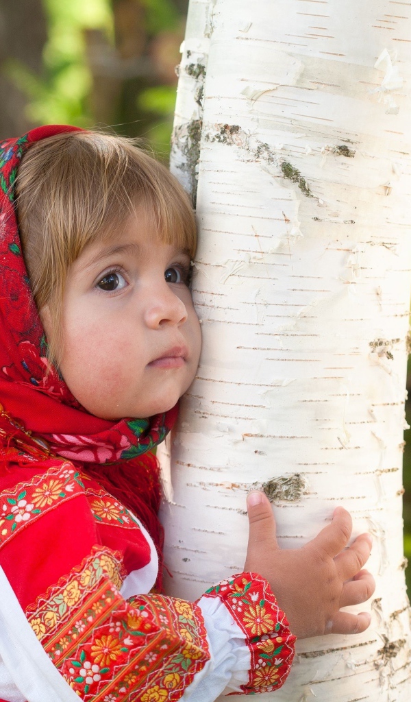 Маленькая девочка в красном платке обнимает березу