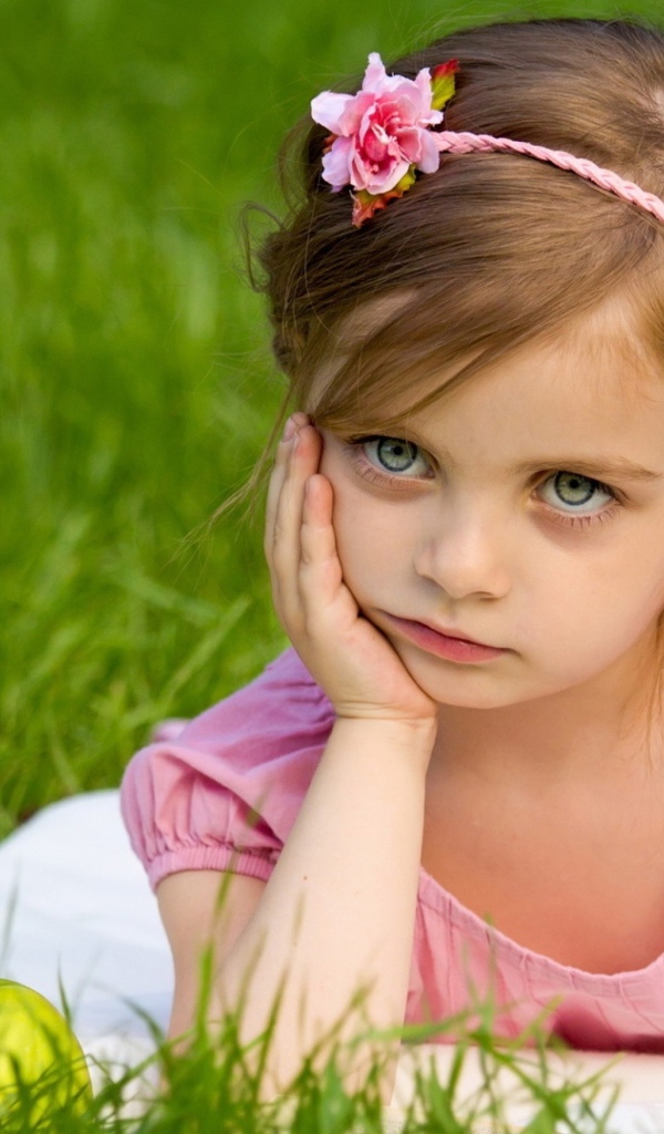 Маленькая девочка в розовом платье лежит на зеленой траве