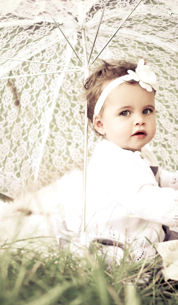 Маленькая девочка сидит на траве с большим белым зонтом