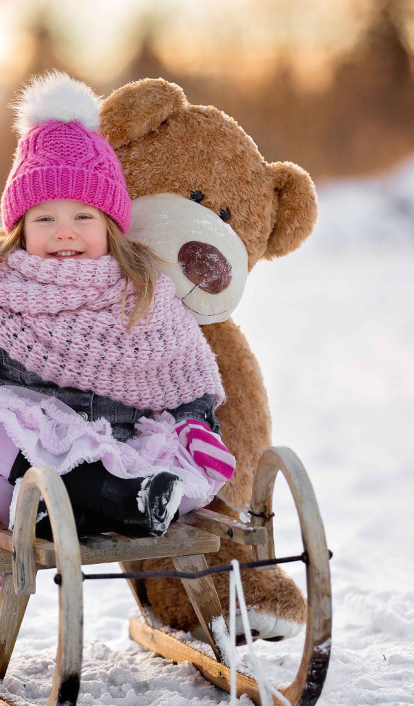 Маленькая девочка на санках с большим медведем зимой 