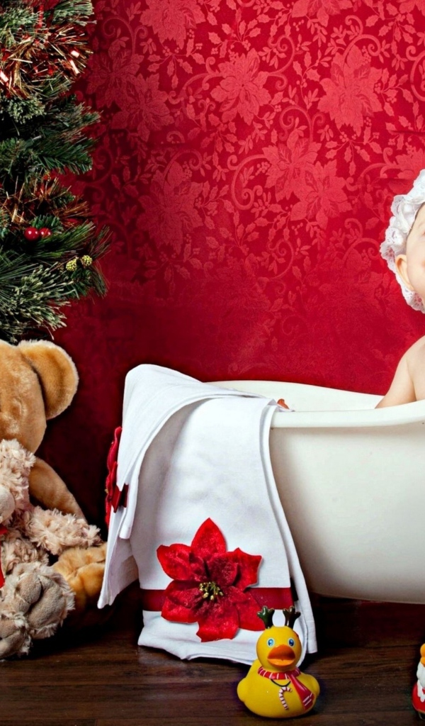 Маленькая девочка сидит в белой ванне у елки с игрушками