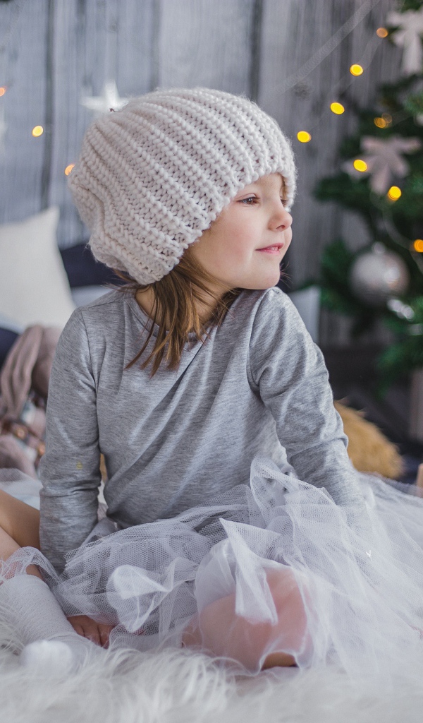 Маленькая девочка сидит на кровати у новогодней елки