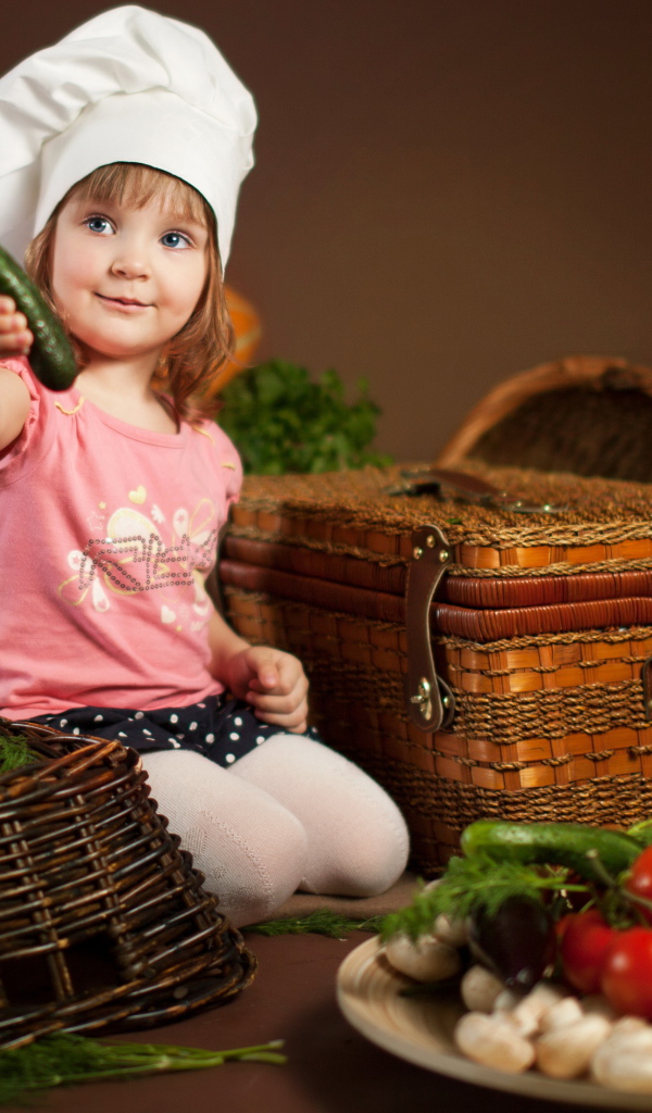 Маленькая девочка сидит на столе с корзинами и овощами
