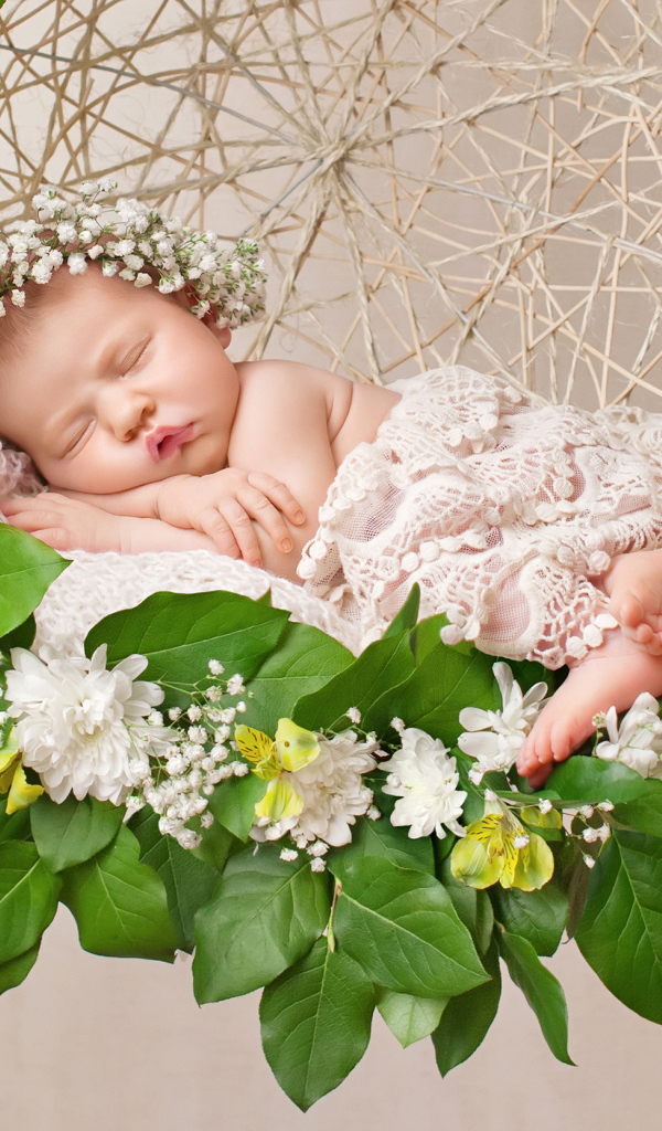 Маленькая девочка спит в колыбеле украшенной зелеными листьями