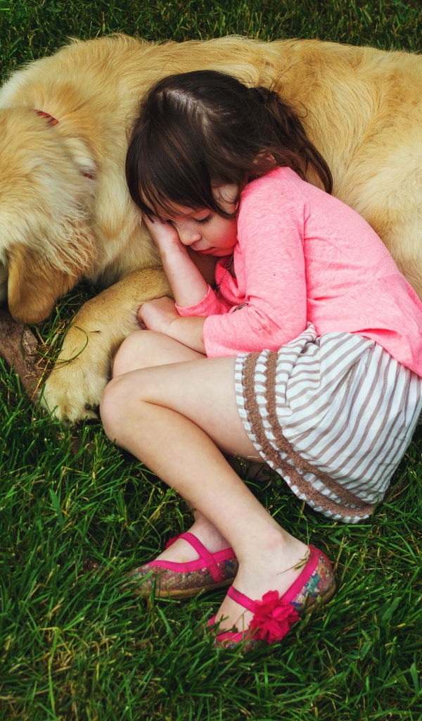 Маленькая девочка спит на зеленой траве с собакой