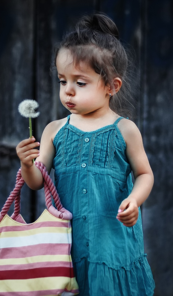 Маленькая девочка с сумкой и одуванчиком в руке