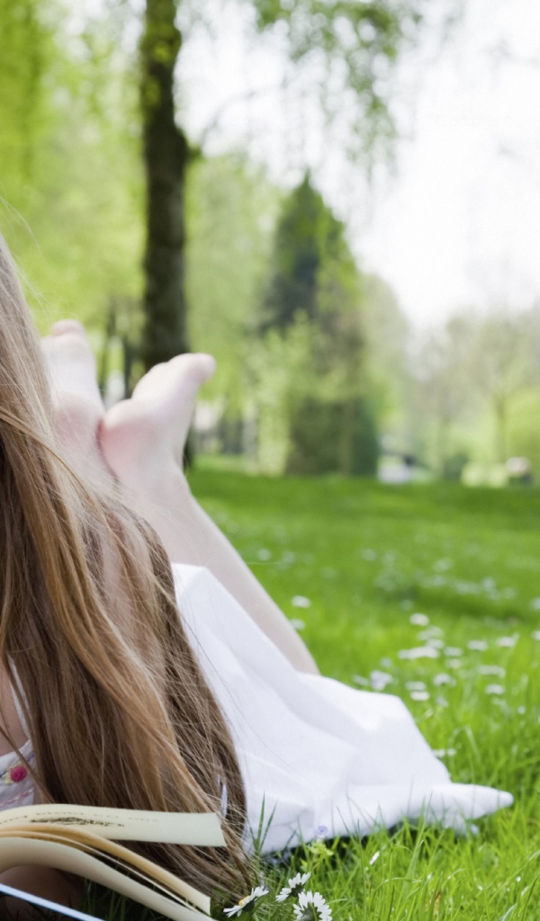 Маленькая девочка с книгой лежит на зеленой траве