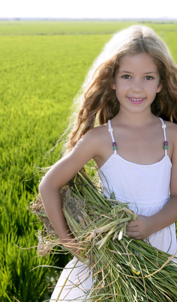 Маленькая девочка с травой в руках на поле