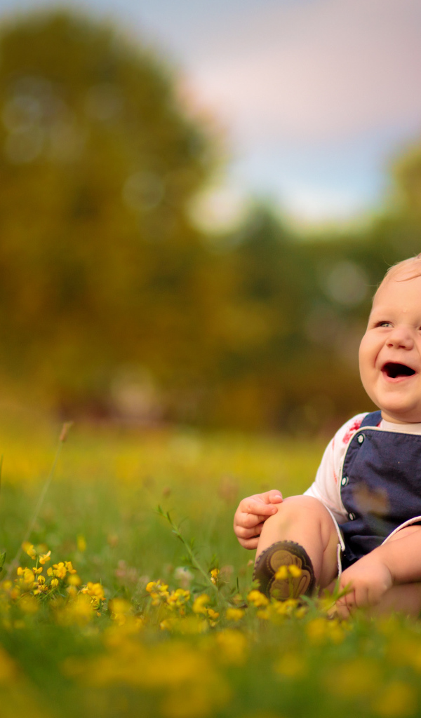 Маленький смеющийся мальчик сидит на траве с желтыми цветами