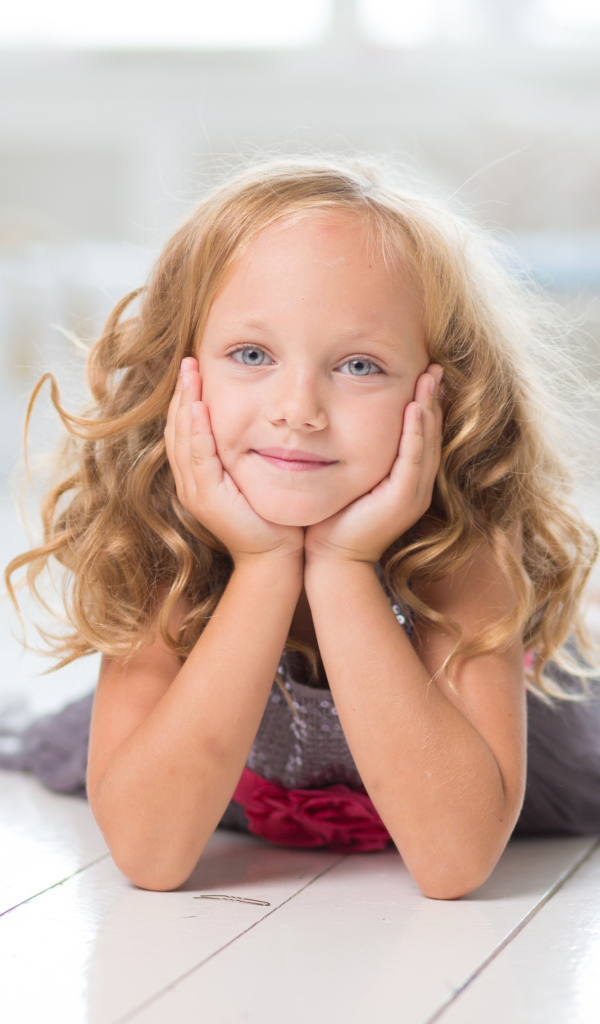 Маленькая длинноволосая голубоглазая девочка лежит на полу