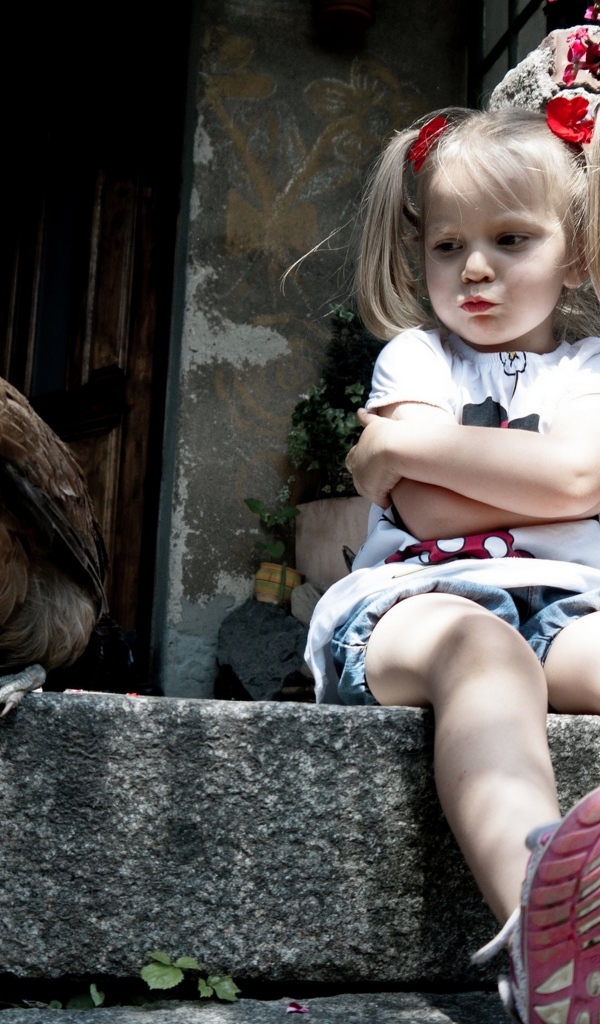 Маленькая обиженная девочка сидит на пороге с курицей
