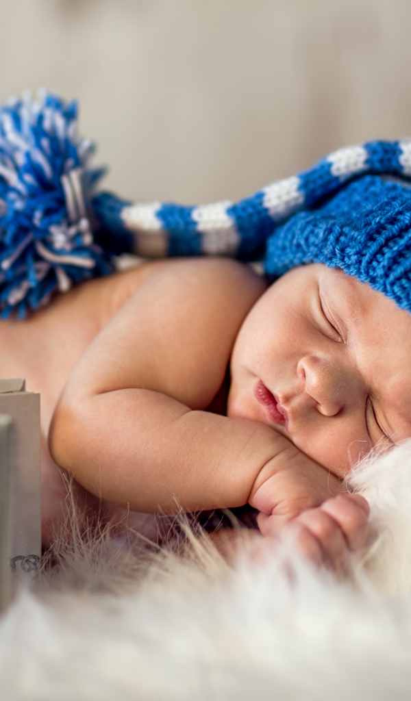Маленький спящий грудной ребенок в синей вязанной шапке 