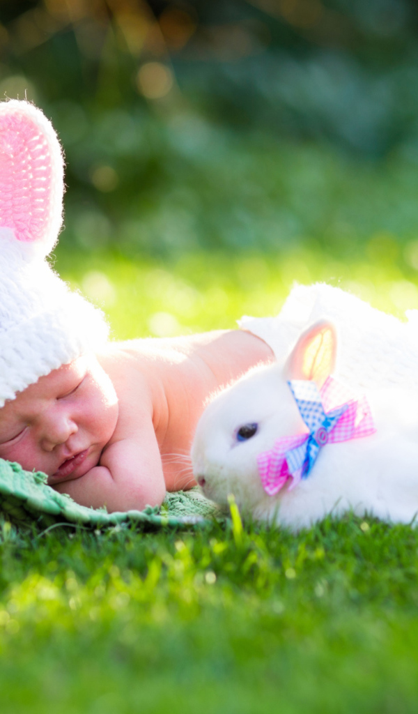 Маленький спящий грудной ребенок на зеленой траве с белым кроликом