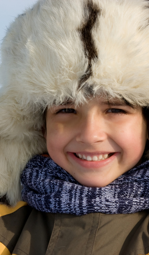 Маленький улыбающийся мальчик в теплой шапке зимой