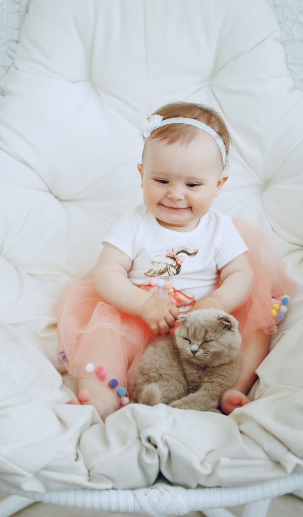Маленький улыбающийся ребенок с котом сидит в белом кресле