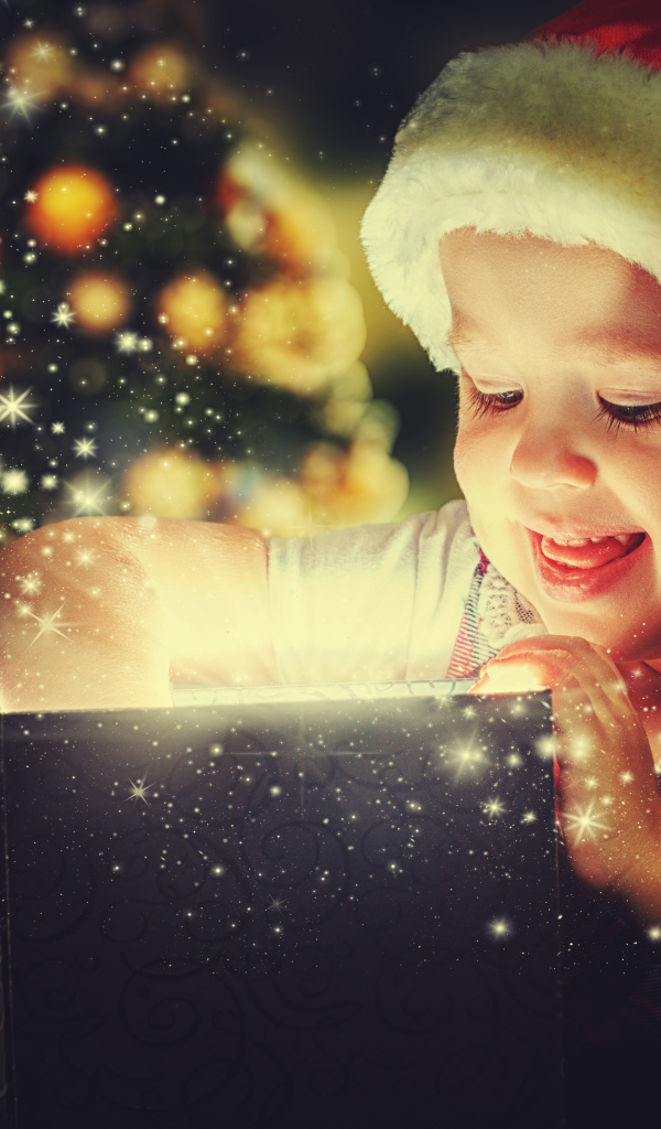 Маленькая улыбающаяся девочка открывает подарок у новогодней елки 