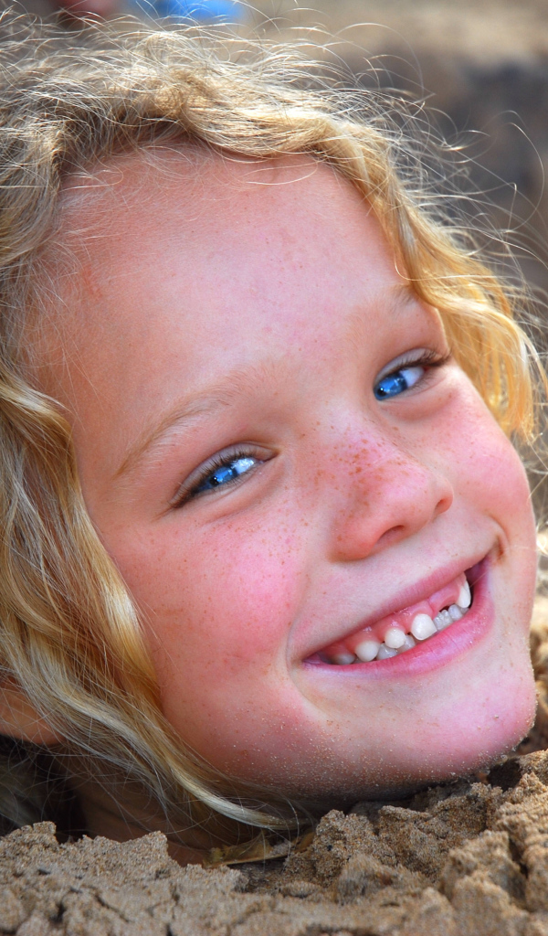 Маленькая улыбающаяся девочка играет в песке