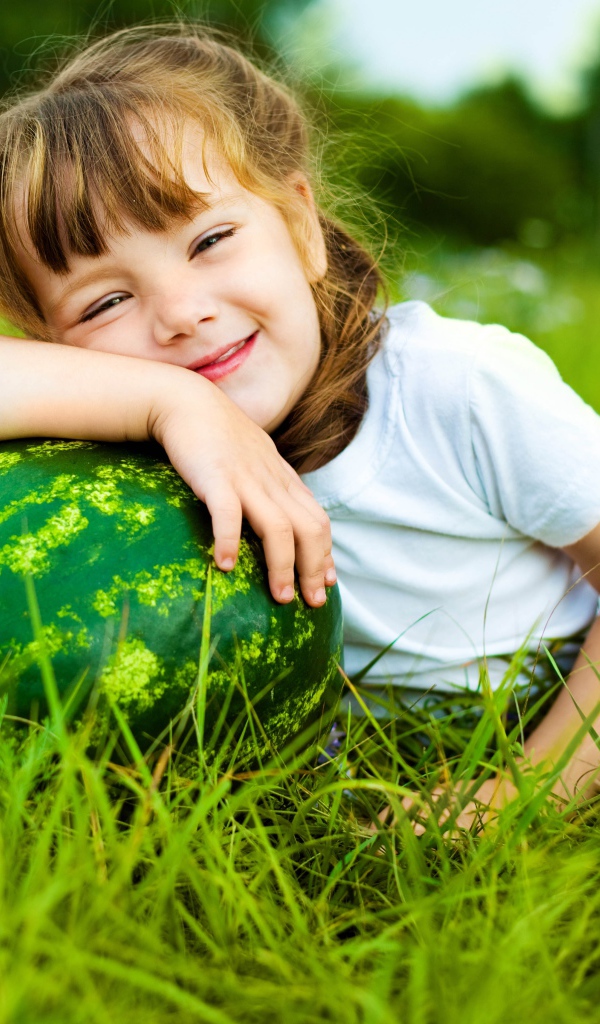 Улыбающаяся девочка с зеленым арбузом на траве