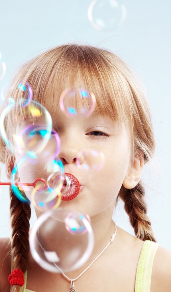 Девочка с косичками пускает мыльные пузыри