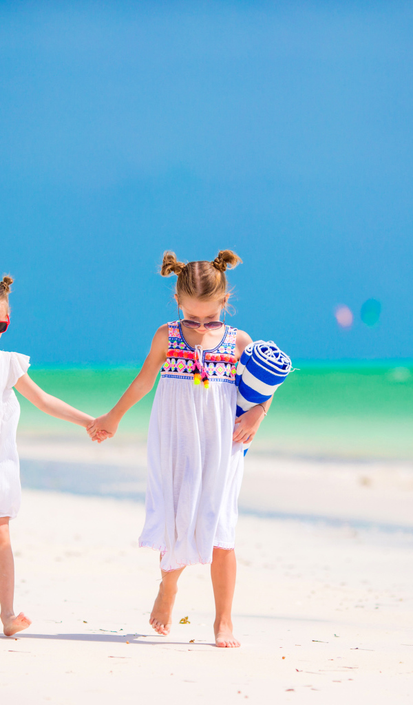 Две маленькие девочки идут по песку