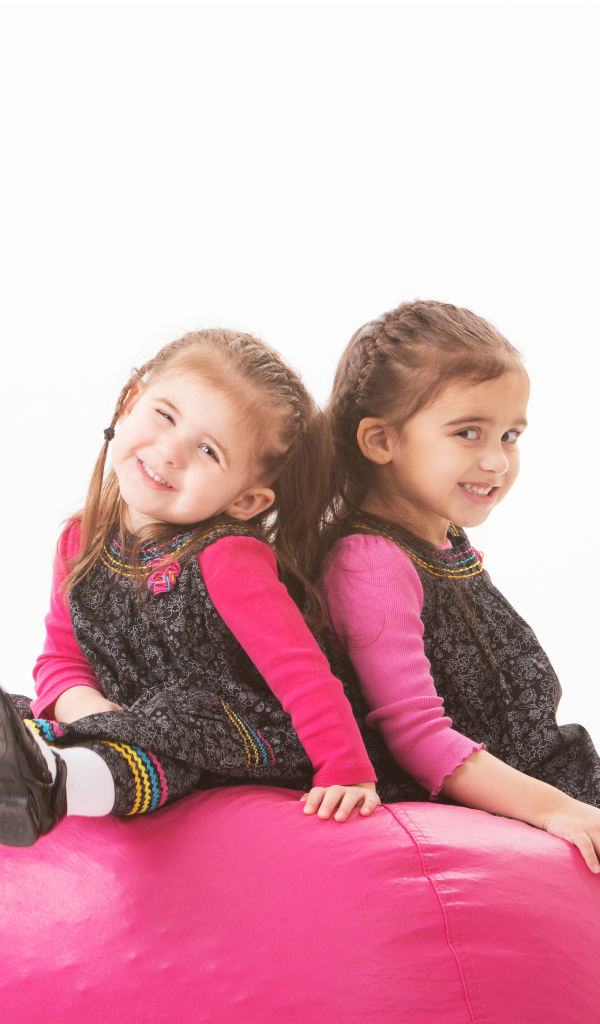 Две маленькие девочки сидят на красном мягком шаре 