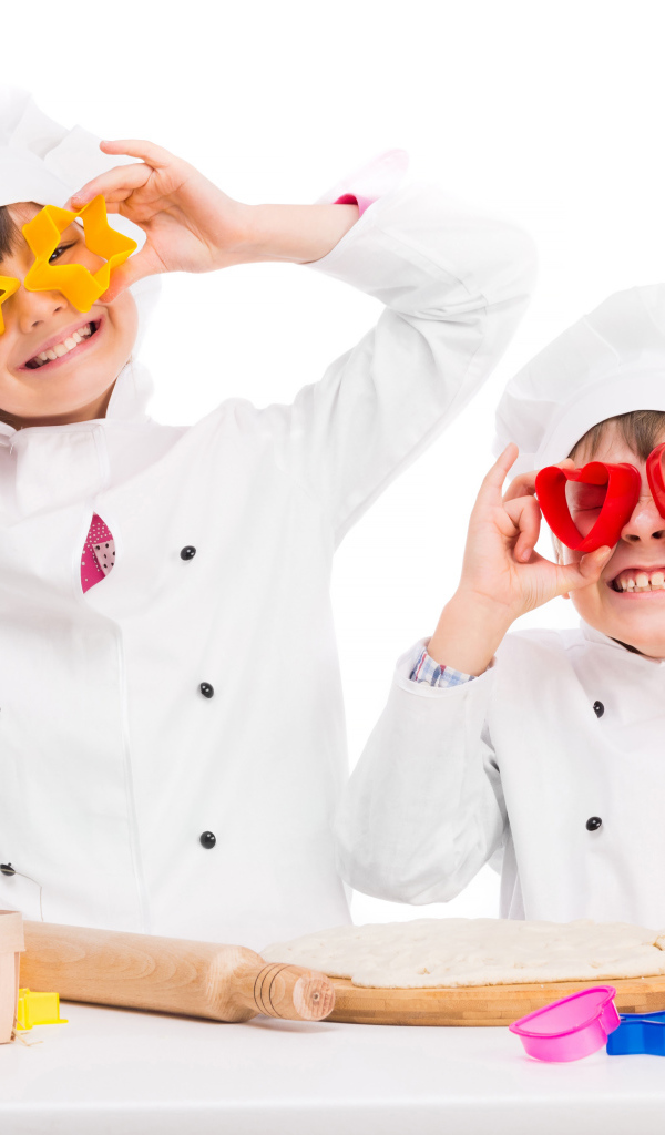 Два маленьких ребенка в костюмах повара готовят на кухне печенье