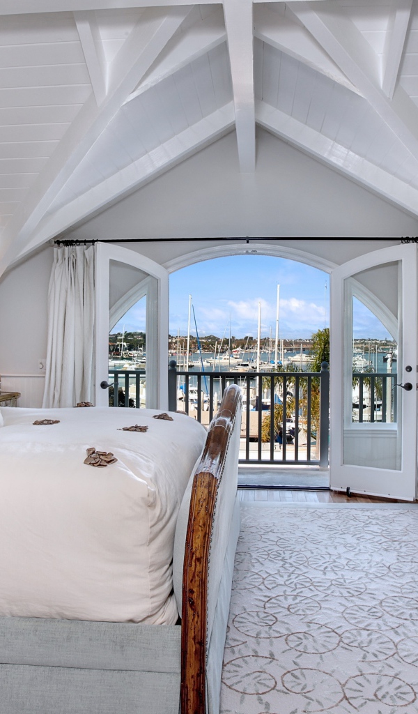 Белая спальня с большой высокой кроватью и балконом 