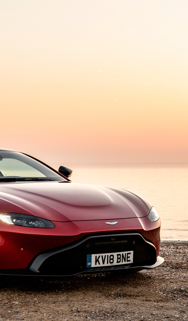 Красный автомобиль Aston Martin Vantage 2019 года на фоне заката у воды