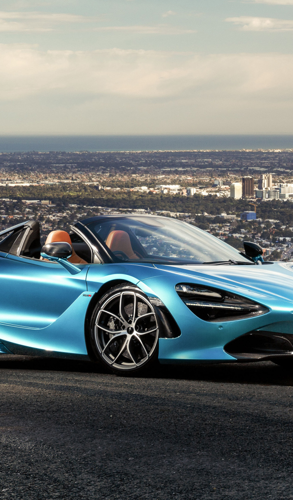 Голубой спортивный автомобиль McLaren 720S Spider 2019 года на фоне города