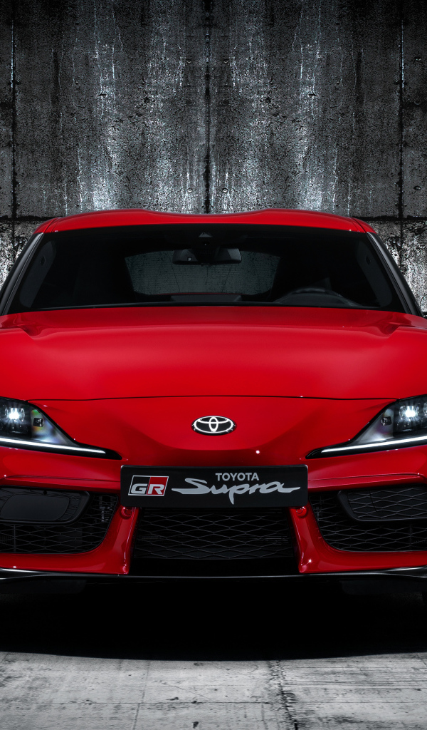 Красный автомобиль Toyota GR Supra 2019 года на фоне серой стены