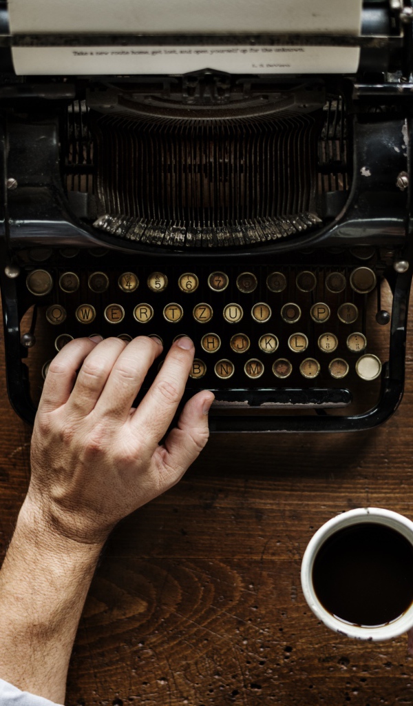 Мужчина с чашкой кофе в руке печатает на старой печатной машинке 