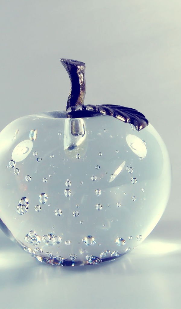 Стеклянное яблоко на сером фоне 