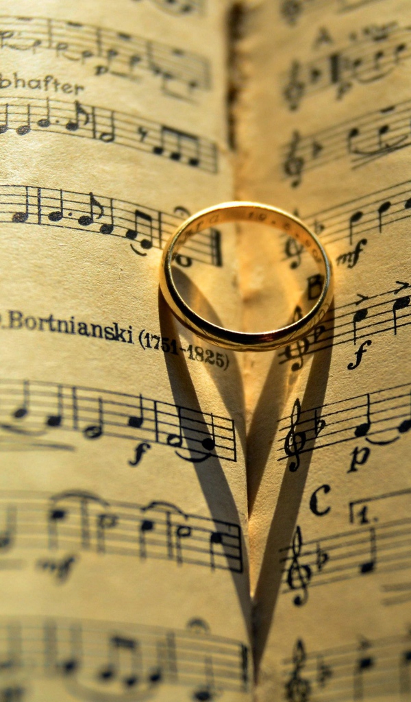 Золотое обручальное кольцо лежит на нотной тетради