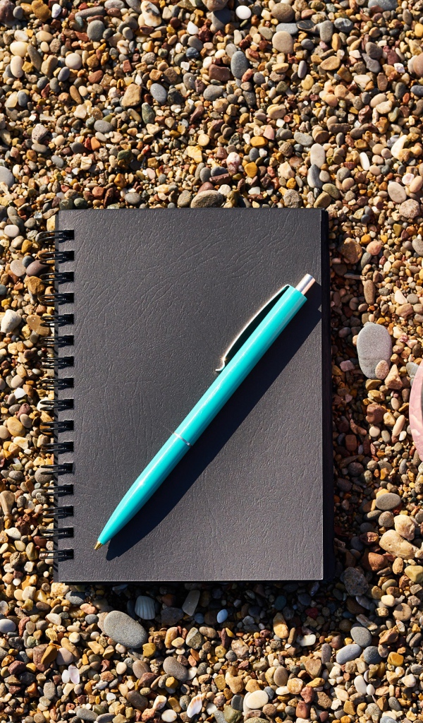 Блокнот с ручкой лет на мелкой гальке с чашкой кофе и красным сердцем 